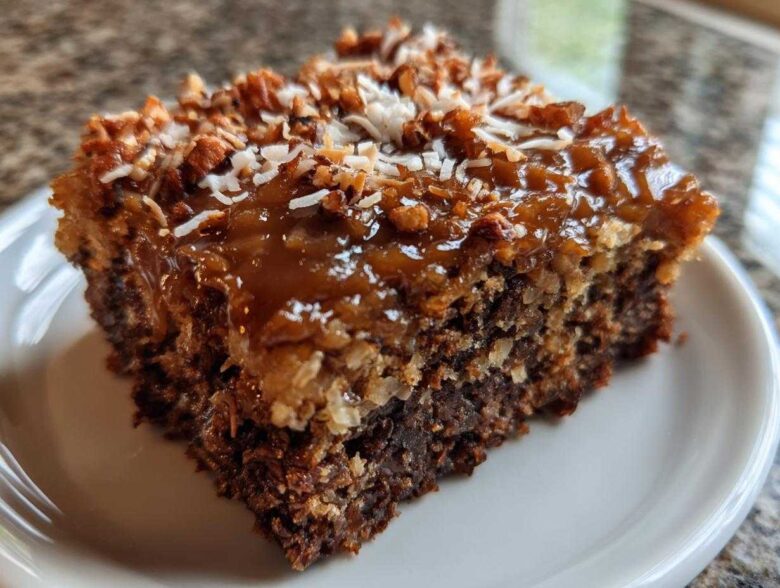 Close-up of a moist slice of german chocolate poke cake topped with gooey caramel, pecans, and coconut.