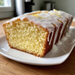 Close-up of a moist lemon pound cake loaf, drizzled with white icing and topped with lemon zest.