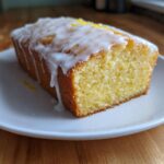 A close-up of a moist slice of lemon pound cake topped with white glaze and lemon zest.