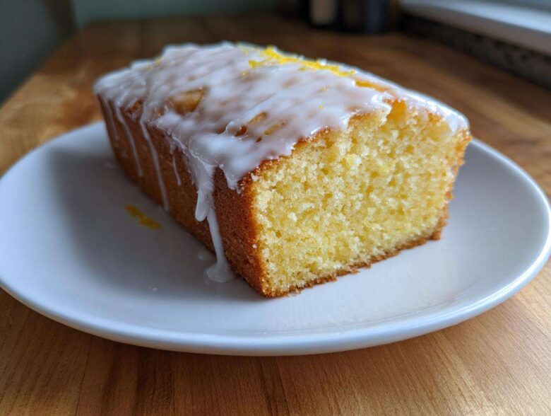 A close-up of a moist slice of lemon pound cake topped with white glaze and lemon zest.