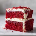 Close-up of a moist, two-layer red velvet cake slice covered in white cream cheese frosting.