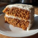 A close-up of a thick slice of moist spice cake with two layers and creamy white frosting.