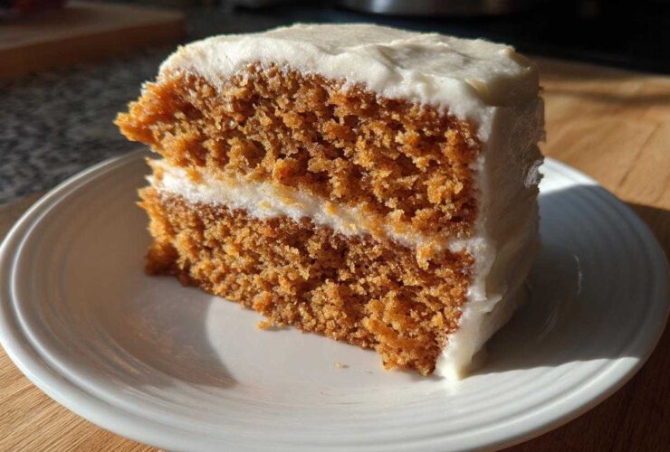 A close-up of a thick slice of moist spice cake with two layers and creamy white frosting.