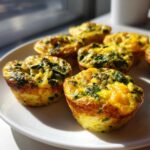 Close-up of several fluffy muffin tin egg bites with visible green spinach pieces on a white plate.