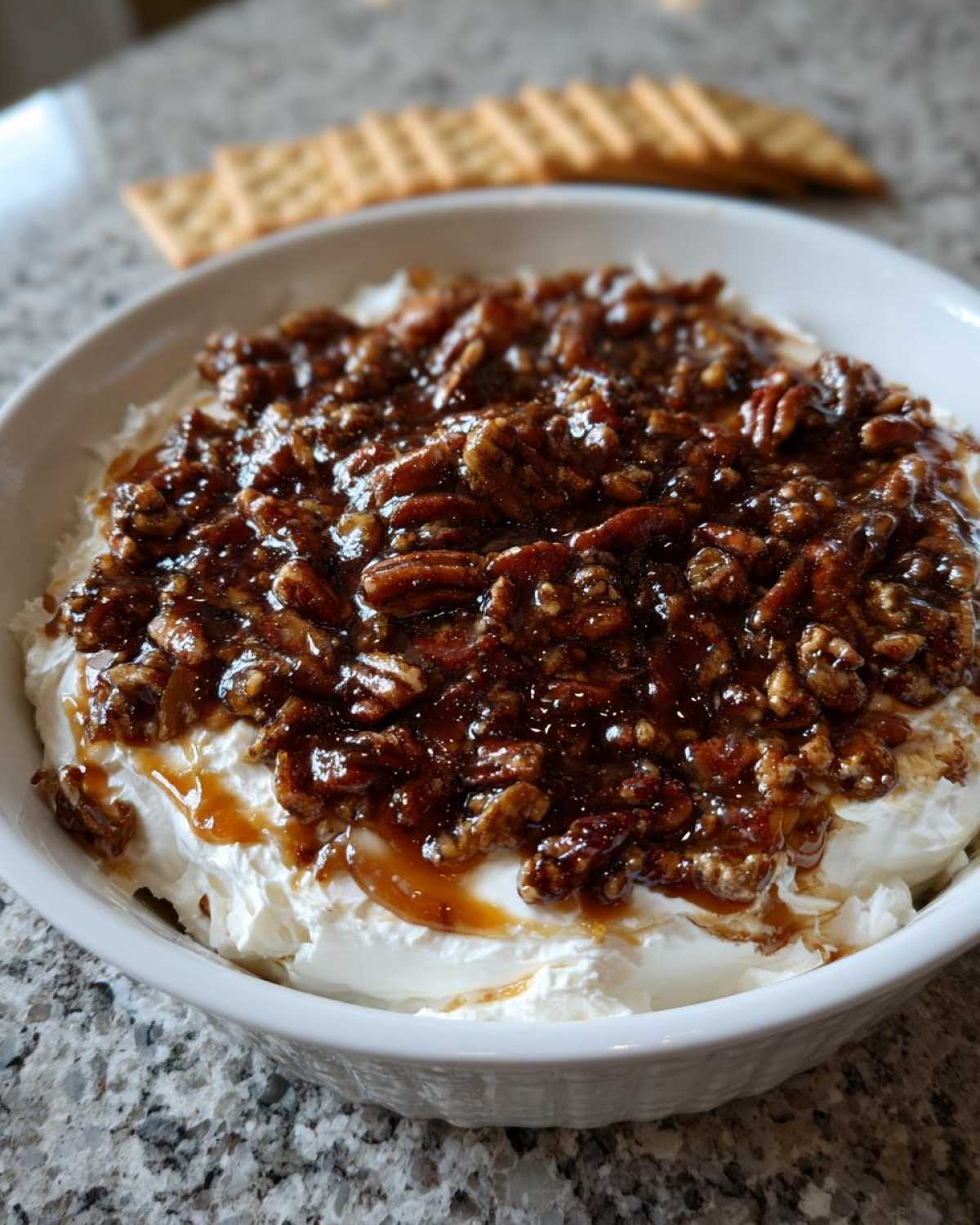 A white bowl filled with no-bake pecan pie dip, topped generously with glazed pecans and caramel sauce.