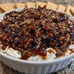 Close-up of a creamy no-bake pecan pie dip topped with sticky caramel and chopped pecans, served with crackers.