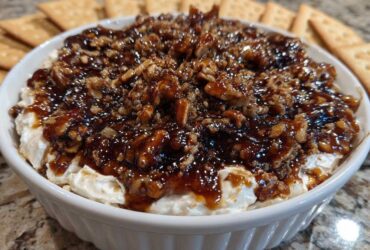 Close-up of a creamy no-bake pecan pie dip topped with sticky caramel and chopped pecans, served with crackers.