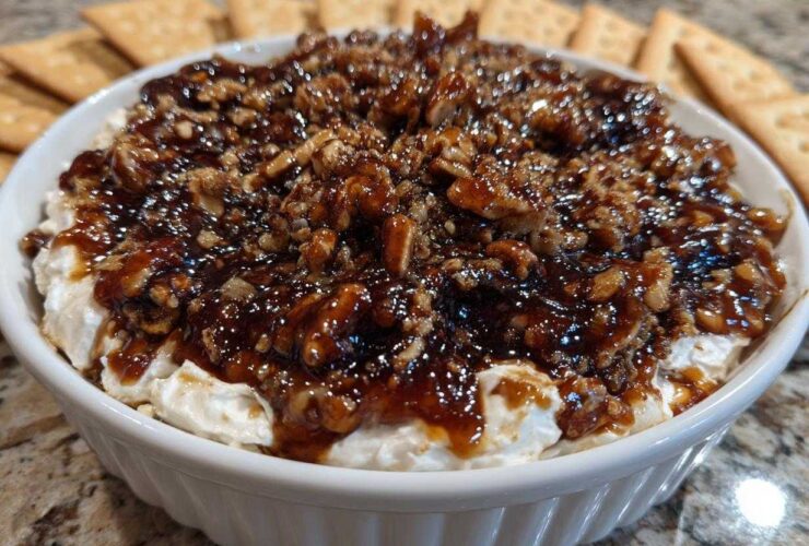Close-up of a creamy no-bake pecan pie dip topped with sticky caramel and chopped pecans, served with crackers.