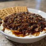 Close-up of creamy pecan pie dip topped with sticky pecans, served with crackers on the side.