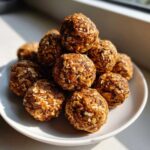 A stack of homemade, no-bake protein balls coated in visible rolled oats, sitting on a white plate.