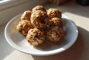 A small pile of homemade, oat-covered protein balls resting on a white plate near a window.