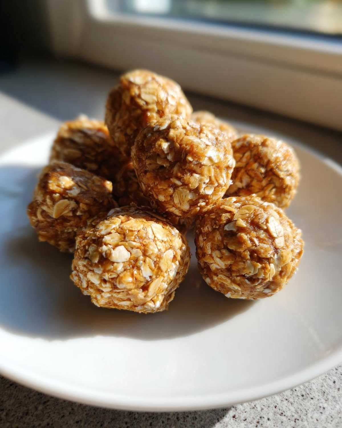 A pile of homemade no bake protein balls coated in visible rolled oats on a white plate.