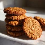 A stack of golden brown oatmeal breakfast cookie with one leaning against the side.