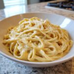 A white bowl filled with fettuccine pasta generously coated in creamy Olive Garden Alfredo Sauce and topped with grated Parmesan cheese.