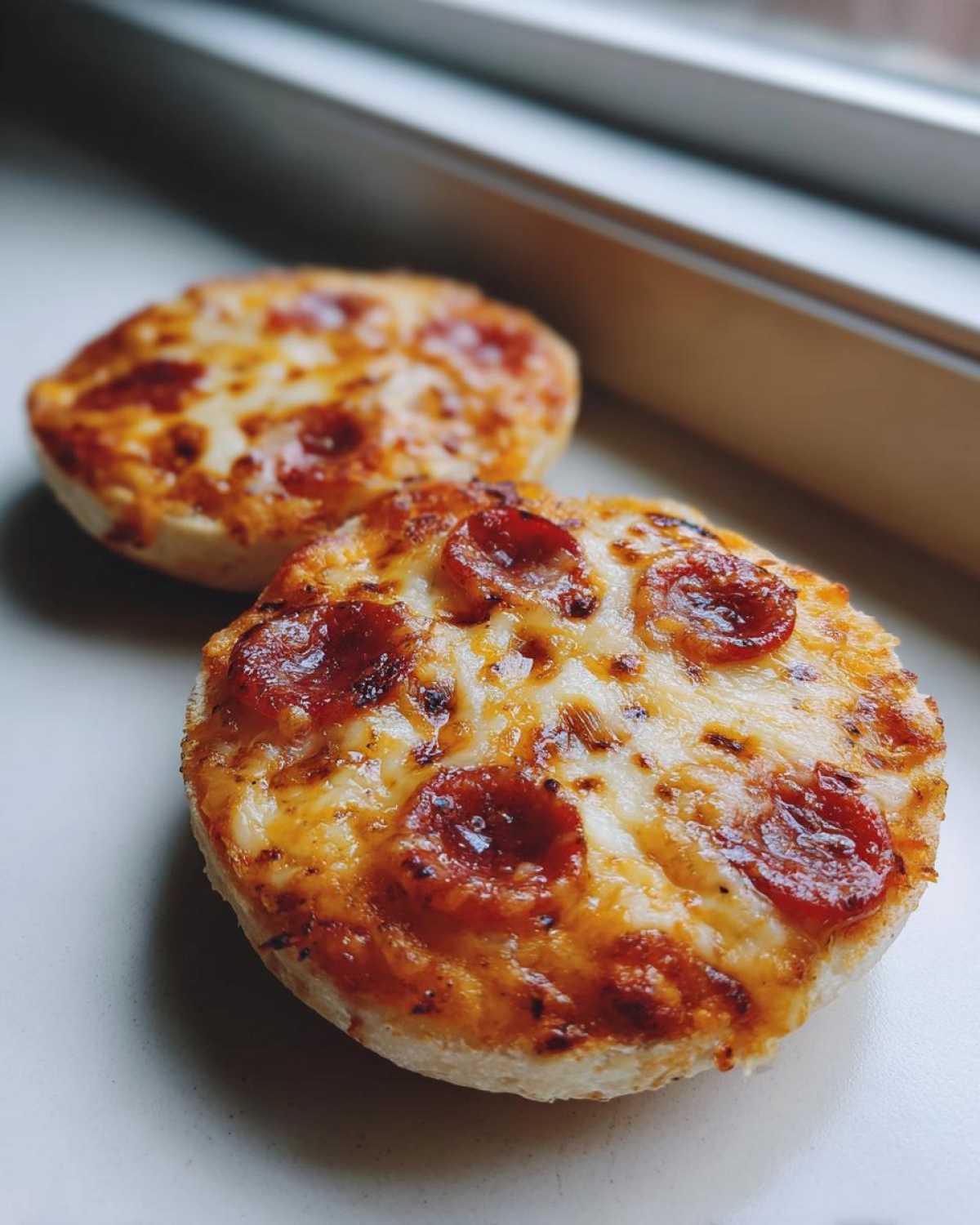 Close-up of two freshly baked pepperoni english muffin pizza halves with melted, bubbly cheese.