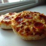 Two freshly baked pepperoni english muffin pizza halves topped with melted, bubbly cheese.