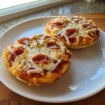 Two freshly baked pepperoni english muffin pizza halves topped with melted cheese and black pepper on a white plate.