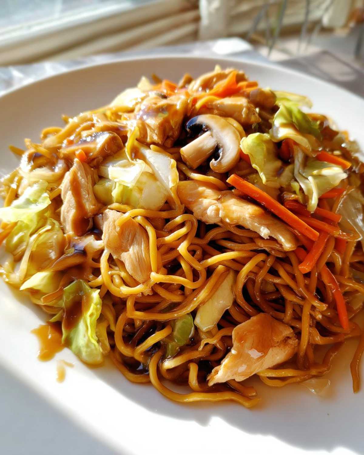Close-up of a serving of delicious chicken chow mein recipe with noodles, chicken pieces, cabbage, carrots, and mushrooms.