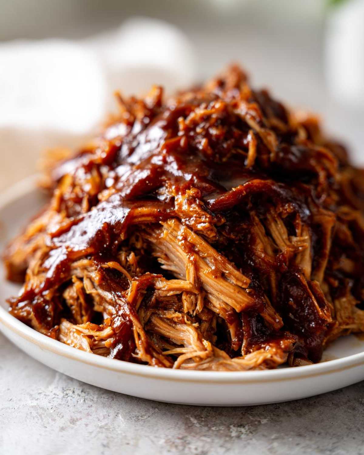 Close-up of tender, shredded pioneer woman slow cooker pulled pork generously coated in dark BBQ sauce.