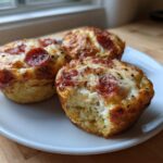 Three golden-brown Pizza Muffins topped with melted cheese and pepperoni slices, served on a white plate.