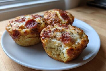 Three golden-brown Pizza Muffins topped with melted cheese and pepperoni slices, served on a white plate.