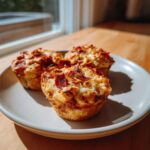 Three freshly baked pizza muffins topped with melted cheese and crispy pepperoni slices on a white plate.