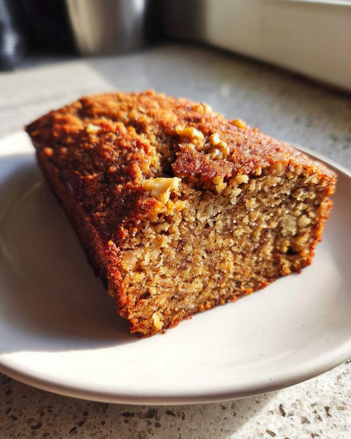 Close-up of a slice of moist protein banana bread topped with walnuts on a white plate.