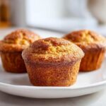 Close-up of three golden brown protein pumpkin muffins resting on a white plate.