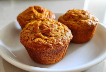 Three golden-brown protein pumpkin muffins sitting on a white plate, ready to eat.