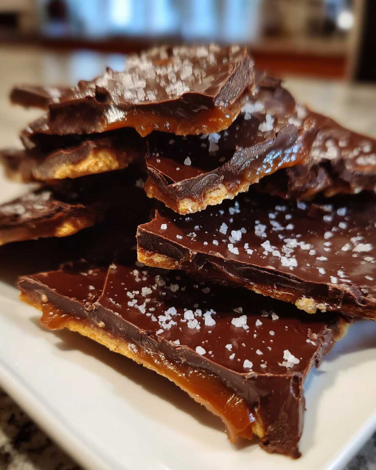 Close-up of broken pieces of saltine cracker toffee topped with melted chocolate and flaky sea salt.
