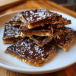 A stack of square pieces of saltine cracker toffee topped with melted chocolate and flaky sea salt.