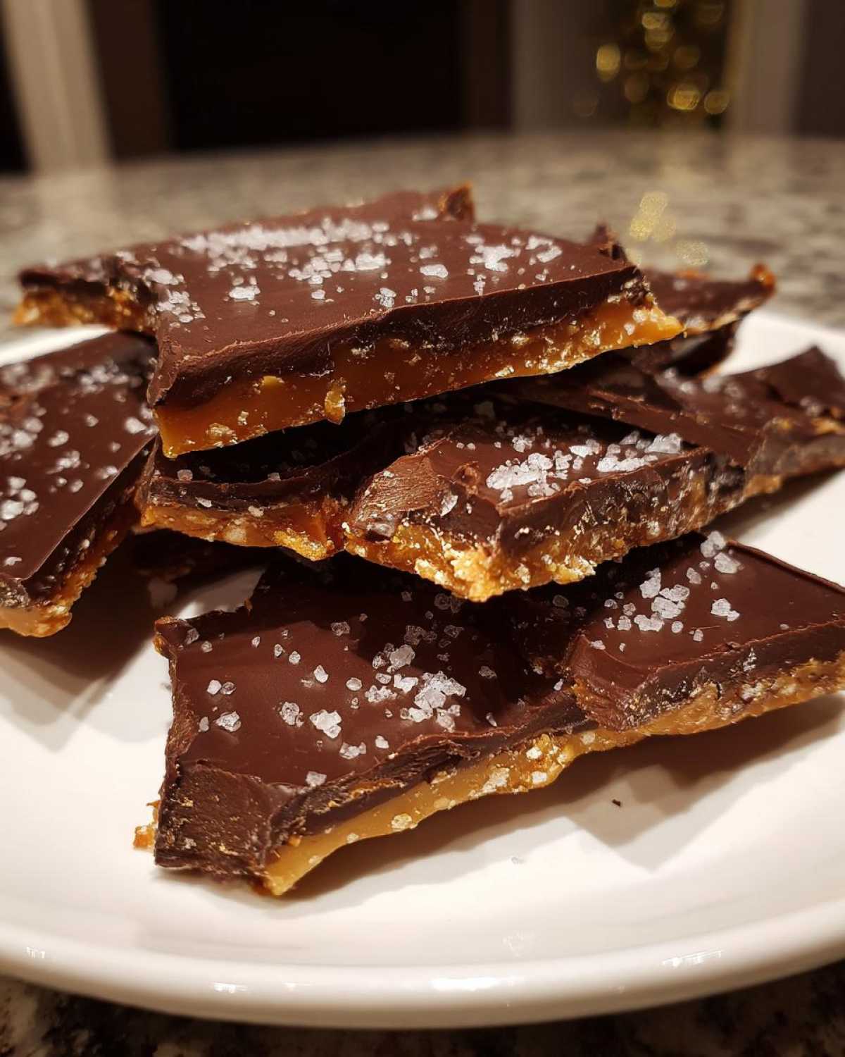 Close-up of broken pieces of saltine cracker toffee topped with melted chocolate and coarse sea salt.