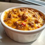 Close-up of hot, bubbly sausage cheese dip topped with melted cheddar cheese in a white bowl.