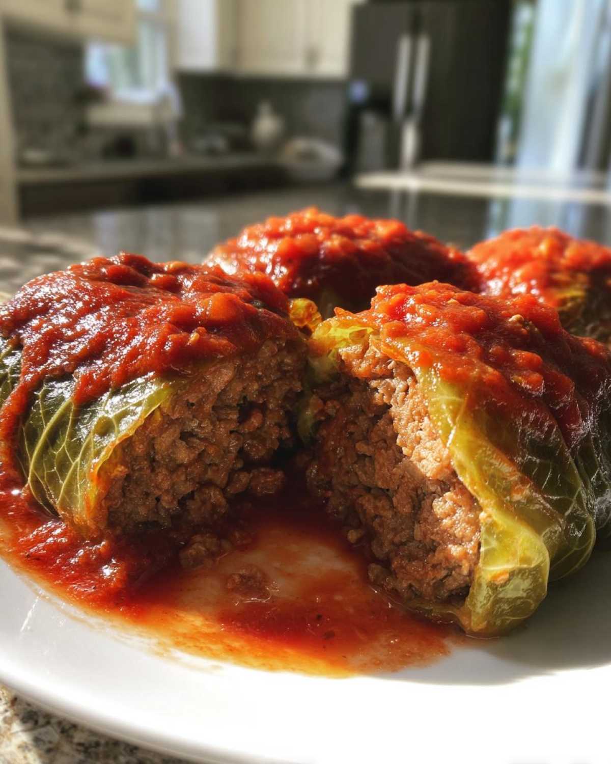 A close-up view of homemade cabbage rolls stuffed with meat, covered in rich tomato sauce, with one roll cut open.