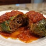 A halved cabbage roll showing the savory meat and rice filling, topped with rich tomato sauce.