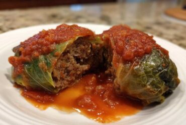 A halved cabbage roll showing the savory meat and rice filling, topped with rich tomato sauce.