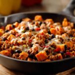 Close-up of a savory sweet potato skillet loaded with ground meat, black beans, peppers, and melted cheese.