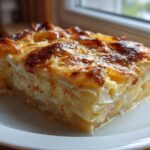 A thick, golden-brown slice of cheesy scalloped potatoes and ham served on a white plate.