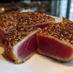 Cross-section view of perfectly seared ahi tuna coated in a sesame seed crust, showing a rare, deep red center.