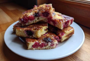 A stack of golden brown sheet pan pancakes squares filled with raspberries and blackberries.