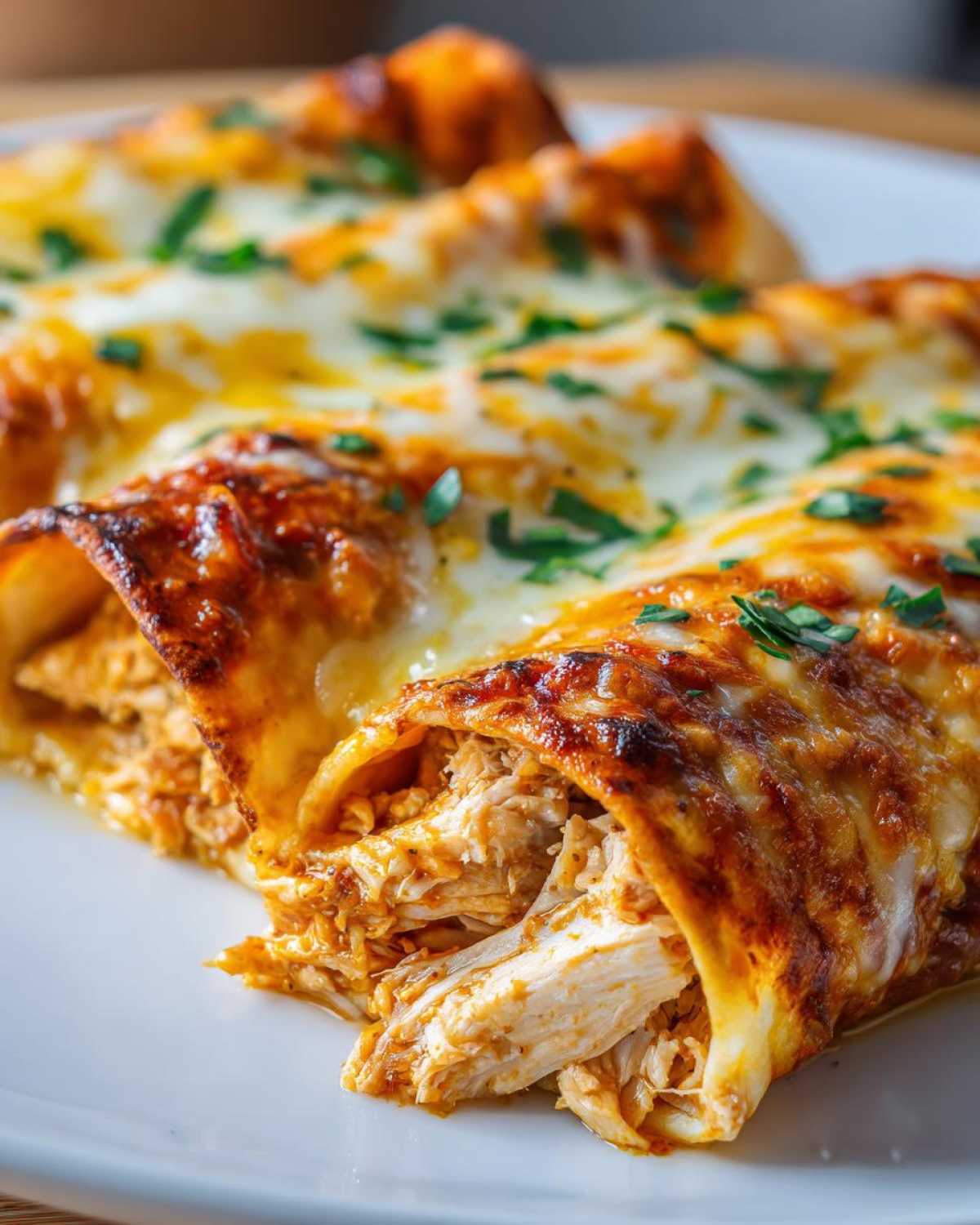 Close-up view of a cheesy green chile chicken enchiladas, showing the shredded chicken filling spilling out.