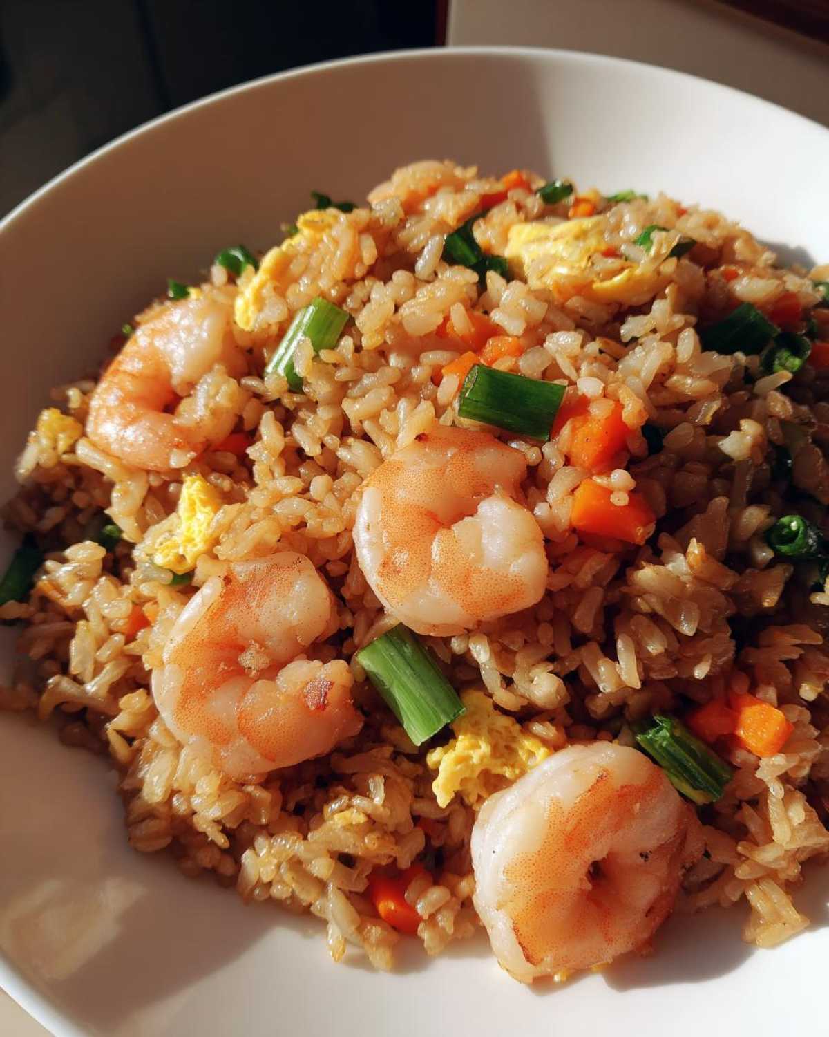 A close-up view of a bowl filled with delicious shrimp fried rice, featuring plump shrimp, scrambled egg, carrots, and green onions.