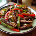 A close-up shot of perfectly cooked steak fajitas featuring strips of seasoned steak mixed with sautéed red and green bell peppers and onions.