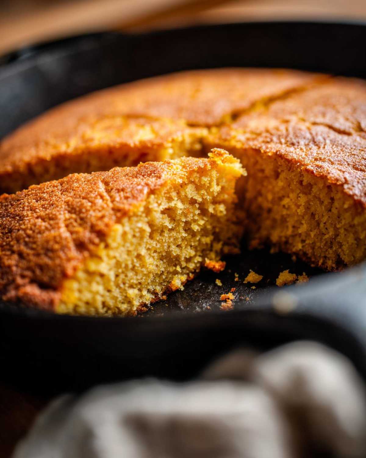 Close-up of a golden slice of moist skillet cornbread cut from the whole loaf in a black cast iron pan.