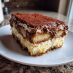 A perfect slice of tiramisu recipe showing layers of cream, coffee-soaked ladyfingers, and a dusting of cocoa powder.