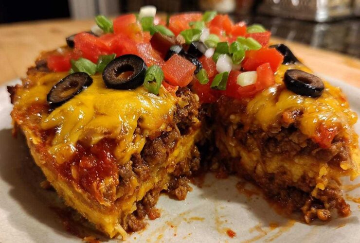 A cross-section slice of homemade Mexican pizza showing layers of seasoned beef, cheese, and topped with fresh tomatoes, olives, and green onions.