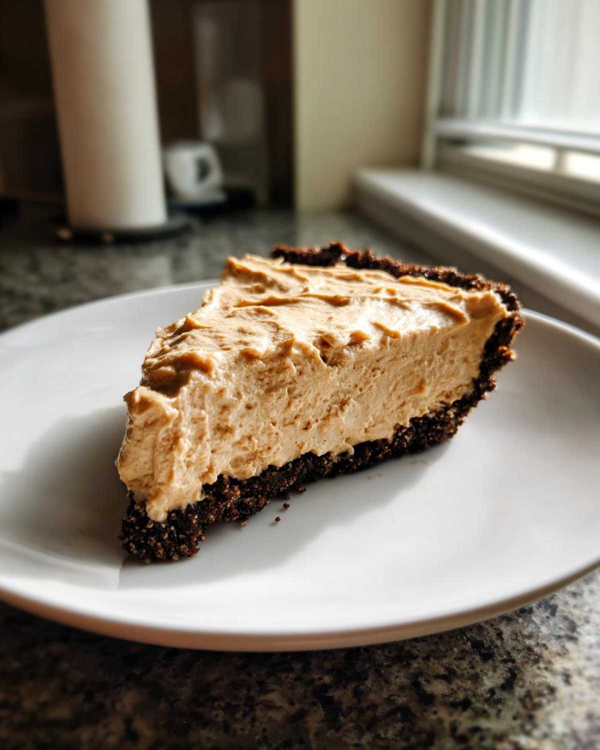 A thick slice of creamy peanut butter pie with a dark chocolate crust served on a white plate.