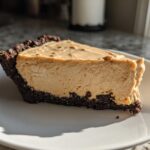A thick slice of creamy peanut butter pie with a dark chocolate crust on a white plate.