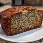 Close-up of a thick slice of moist protein banana bread showing nuts and banana flecks on a white plate.