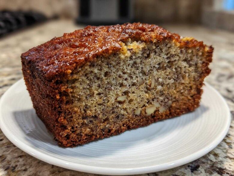 Close-up of a thick slice of moist protein banana bread showing nuts and banana flecks on a white plate.